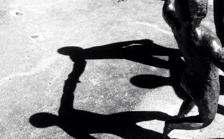 Decorative black and white photo of shadows of a small statue of people in a circle on concrete